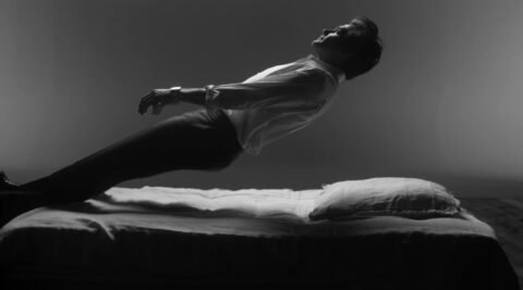 Homme en chemise blanche tombant en arrière sur un lit, en noir et blanc