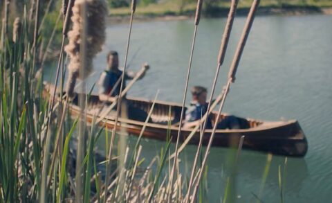 Tranquil moments on the water: a pair of individuals enjoy a leisurely canoe ride amidst the serene backdrop of a calm lake, framed by the whispering reeds at the water's edge.