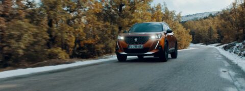 Voiture Peugeot roulant sur une route entourée d'arbres automnaux.