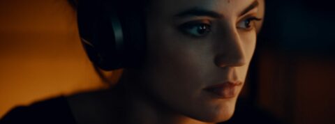 Femme portant un casque audio, concentrée, avec un éclairage ambiant chaud.