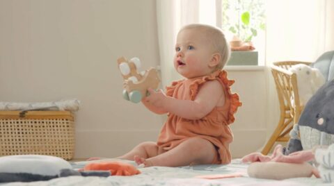 Bébé jouant avec un jouet en bois, assis sur le sol dans une pièce lumineuse
