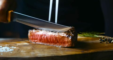 Couteau tranchant une pièce de viande sur une planche à découper.