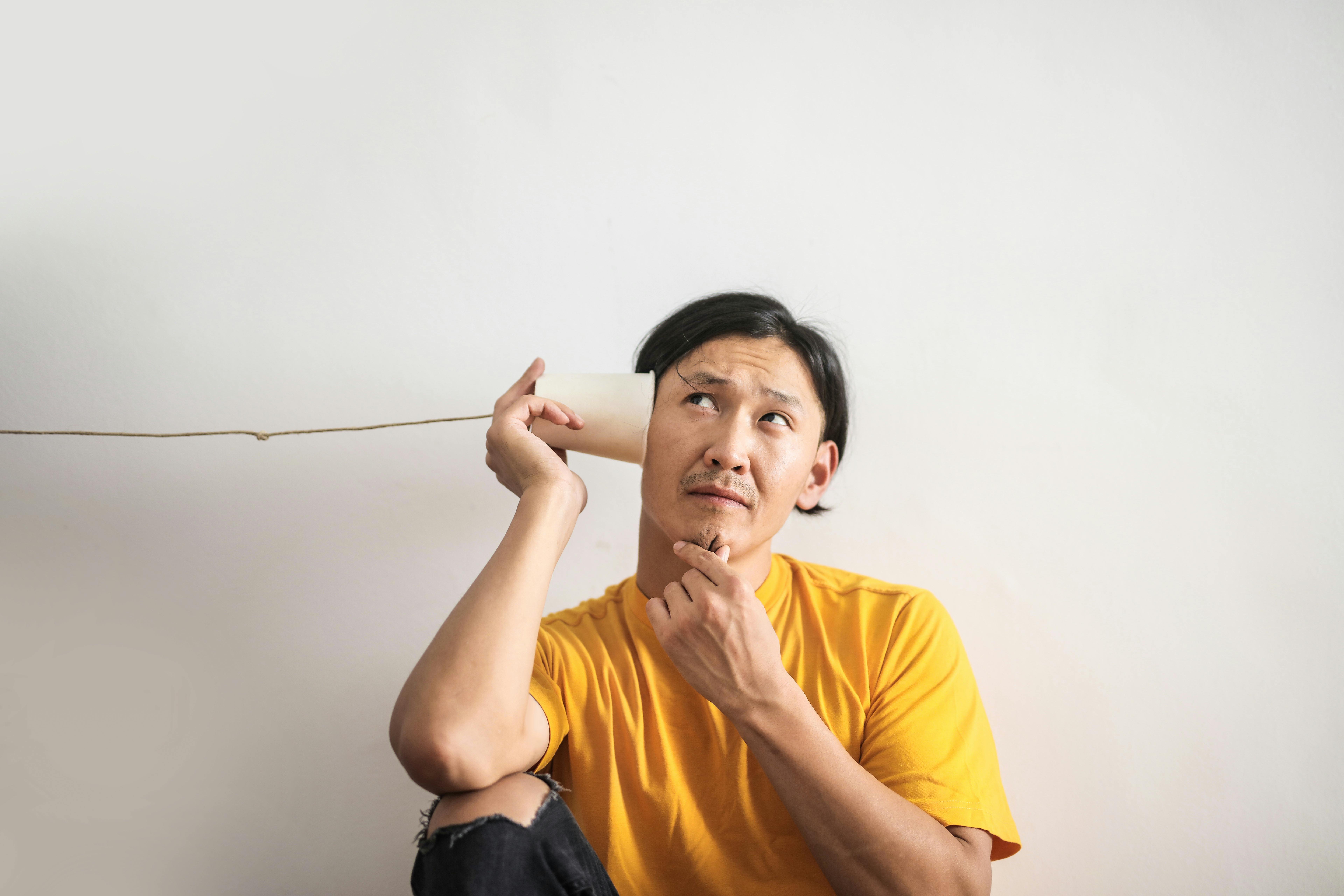 Homme en t-shirt jaune utilisant un téléphone en gobelet, l'air pensif.