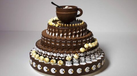 Gâteau en chocolat à plusieurs étages décoré de motifs de pop-corn et d'une tasse en chocolat sur le dessus.