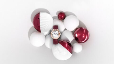 Une montre avec un bracelet rouge et un cadran rond, entourée de sphères blanches et rouges disposées artistiquement sur un fond blanc.