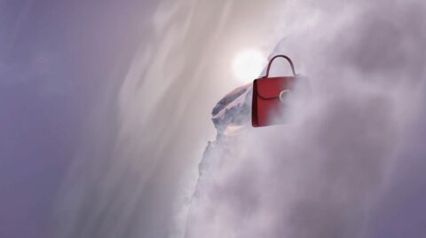 Un sac à main rouge flotte parmi les nuages avec un sommet de montagne enneigé en arrière-plan.