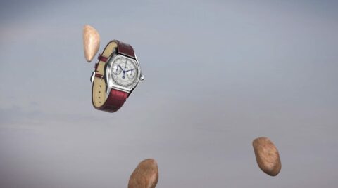 Une montre-bracelet avec un bracelet en cuir rouge flotte parmi des pierres sur un fond de ciel clair